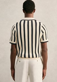 Kratka-samostojna pulover z stripe v krem in mornarsko modri, z rebrastim ovratnikom in teksturiranim pletenjem. Dopolnjujejo ga bele hlače.
