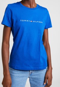 Modré bavlněné tričko s kulatým výstřihem, krátkými rukávy a bílým logem "TOMMY HILFIGER" na hrudi pro branding.