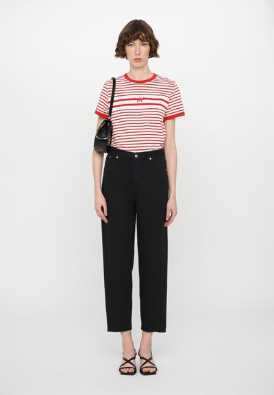 Striped red and white t-shirt with a black graphic, paired with high-waisted black trousers and black strappy sandals, holding a black bag.