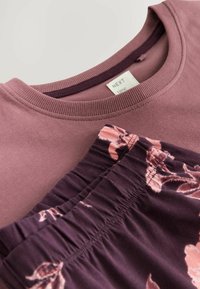 Mjuk lila T-shirt med ribbad krage, tillsammans med mönstrade mörklila byxor med ljusa blommönster och midja med rynk.