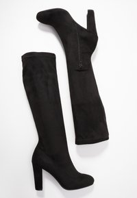 Botas de ante negras por encima de la rodilla con un alto tacón bloque, que cuentan con un cierre de cremallera en el lado interior y una textura mate suave.