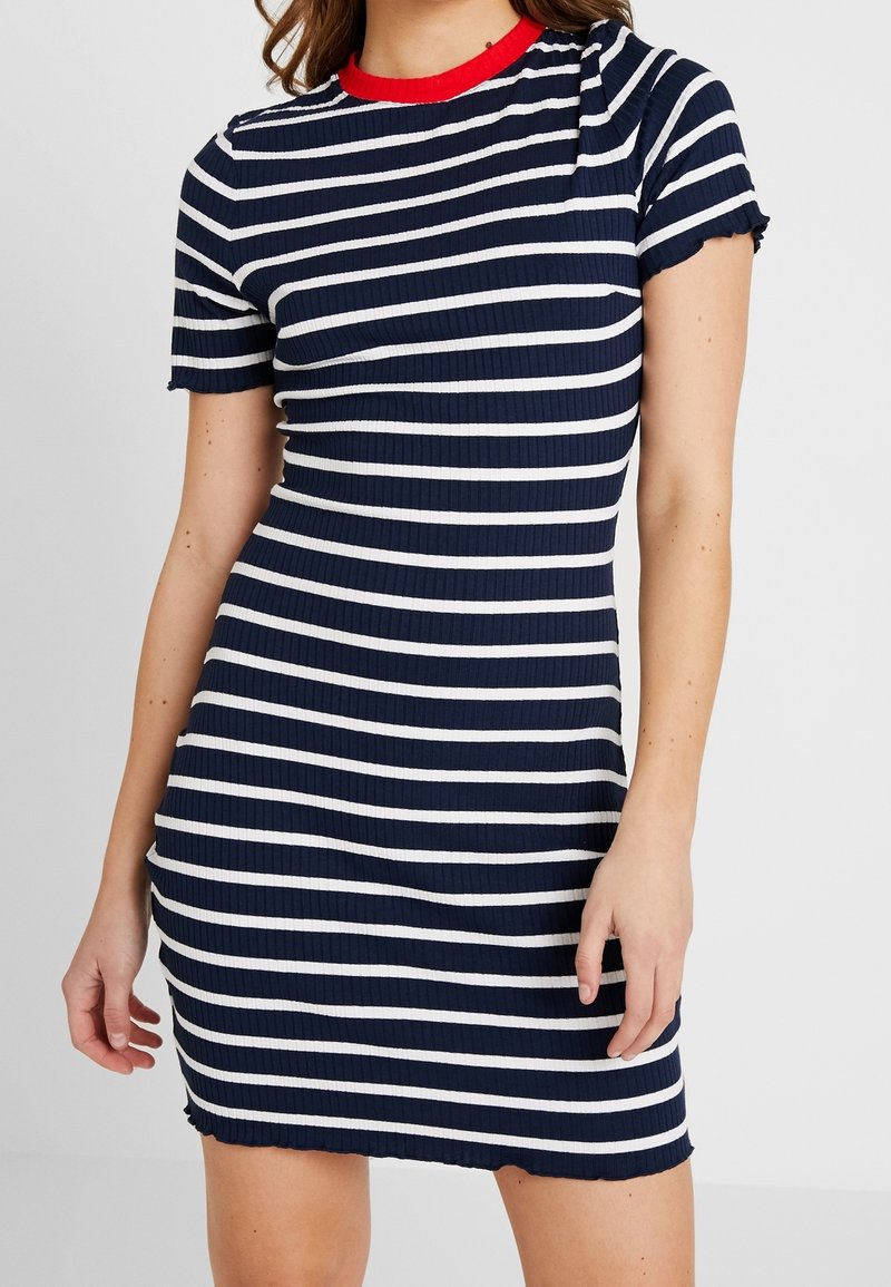 Granatowa i biała sukienka w paski o prążkowanej fakturze, z krótkimi rękawami i okrągłym czerwonym dekoltem. Charakteryzuje się dopasowanym krojem z postrzępionym dołem.