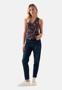 Mouwloze, marineblauwe bloemen-top met knoopsluiting, textuurstof, gecombineerd met donkerblauwe jeans en witte sneakers.