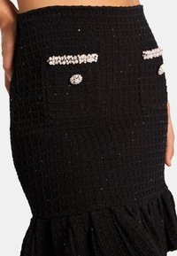 Jupe noire texturée avec un motif à carreaux, dotée de deux poches ornées d'embellissements ressemblant à des perles et d'un ourlet festonné.