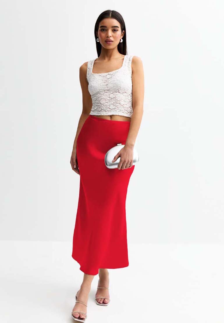 Top corto in pizzo bianco con scollo quadrato abbinato a una gonna midi rossa aderente. Il modello tiene una pochette argentata e indossa sandali con tacco trasparente.