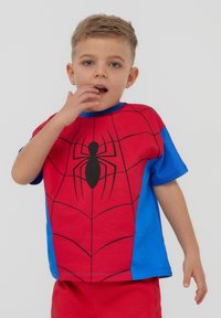T-shirt di cotone rosso e blu con un design di Spider-Man che presenta un silhuette di ragno nero. Maniche corte e scollatura rotonda.