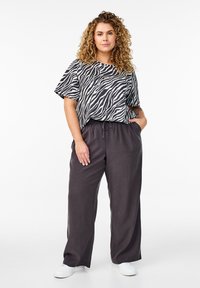 Černobílá zebra pruhovaná krátká rukávová trička v kombinaci s volnými tmavě šedými kalhotami. Model má na sobě bílé tenisky.