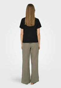 Svart kortärmad topp, avslappnad passform; i kombination med ljus olivgrön, vida byxor med struktur. Utsikten visar baksidan av outfiten.