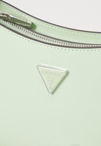 Sac à main en simili cuir vert menthe avec un emblème triangulaire en métal argenté et une fermeture éclair avec des détails en métal argenté.