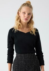 Suéter negro de punto con cuello en V y puños acanalados, combinado con una falda estampada en blanco y negro con un tejido texturizado.
