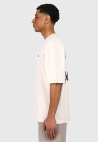 Kortærmet, cremefarvet t-shirt med en løs pasform og sort tekstgrafik på ryggen. Blødt stof, afslappet form, simpelt design.