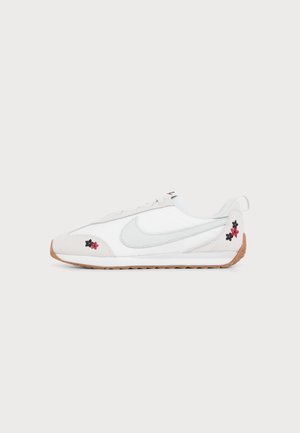 Baskets blanches Nike avec un swoosh gris clair, semelle en gomme et petite broderie florale rouge et noire près des orteils et du talon.