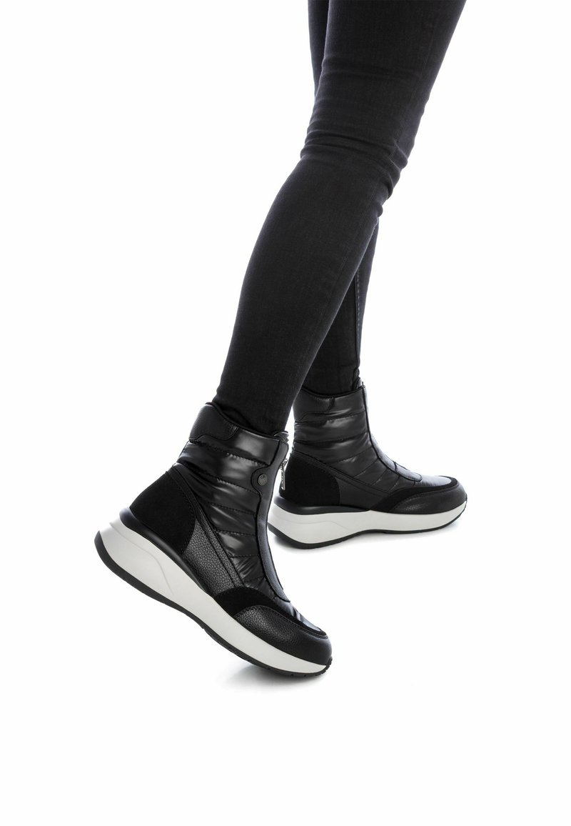Stivali alla caviglia imbottiti neri con tomaia in pelle testurizzata e sintetica, caratterizzati da una suola bianca e un design elegante, che enfatizzano comfort e supporto.