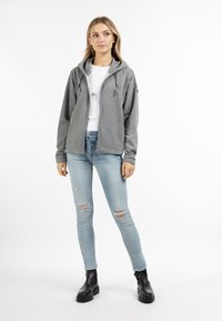 Szürke zipzáras kapucnis pulóver, hosszú ujjakkal és oldalsó zsebekkel. Világoskék, koptatott skinny farmerrel és fekete bokacsizmával párosítva.