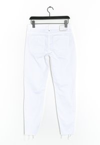 Jeans skinny de mezclilla blanca con dobladillo desgastado, dos bolsillos traseros y una etiqueta en la cinturilla, colgados en un gancho negro.