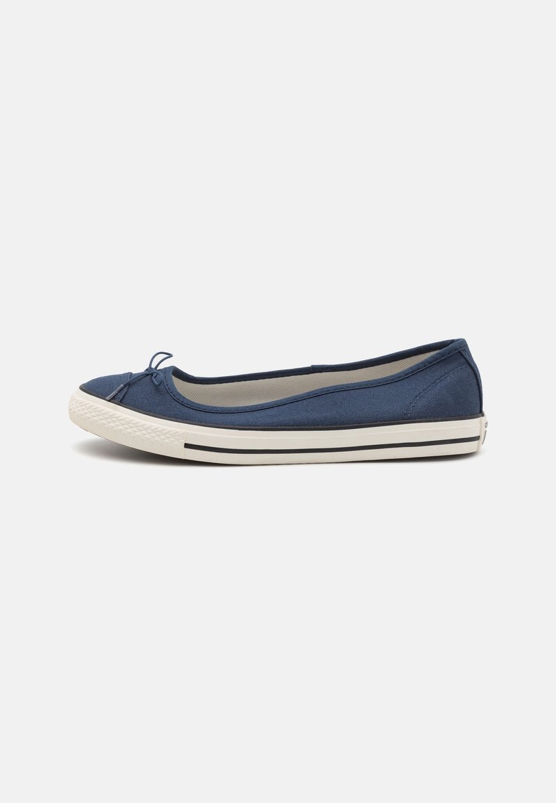 Ballerine en toile bleu marine avec semelle en caoutchouc blanche, détail de bande noire et petit nœud sur le bout, présentée de profil sur fond blanc.