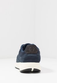 Námořnické modré semišové tenisky s texturovaným zadním opěrkou, bílou mezipodešví a černou podešví s jemným tečkováním.