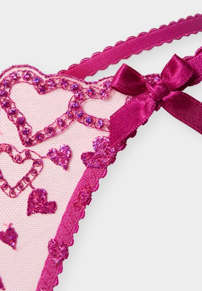 Tissu en dentelle rose avec des cœurs brodés et des strass, décoré d'un nœud en satin magenta brillant et d'une bordure à bords festonnés.