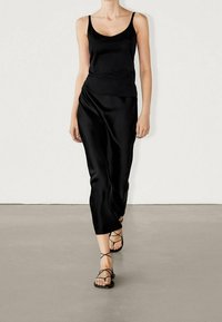 Sort satin tank top bundet med en lang sort satin nederdel. Modellen bærer strappy sorte sandaler. Glat tekstur, enkelt design, ingen mønstre.