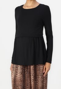 Svart långärmad topp i mjukt tyg med samlad midja; kombinerad med en leopardmönstrad plisserad kjol. Enkel rund halsringning, figursydd bodice.