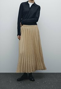 Vaaleanbeige laskoshame, jossa on leveä vyötärö, yhdistettynä tummansiniseen pitkähiharaiseen polo-paitaan. Mustat kengät täydentävät asun.