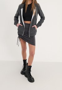 Sudadera gris con cremallera y forro interior blanco, combinada con una falda mini arrugada de color gris oscuro y botas de combate negras brillantes con cordones.