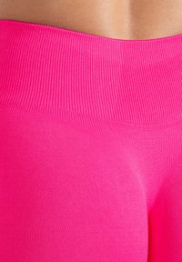 Jasnoróżowe legginsy z teksturowanym, prążkowanym pasem w talii i gładką częścią główną. Materiał wydaje się elastyczny i dopasowany do sylwetki.