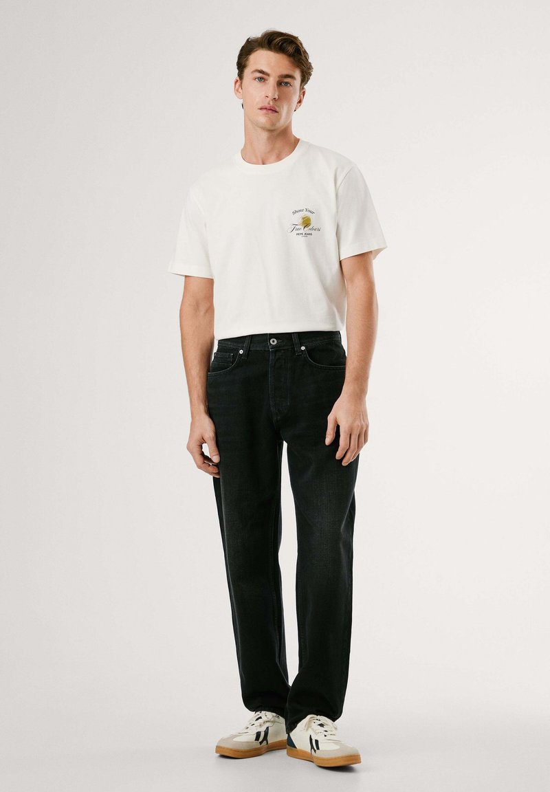 Camiseta de algodón blanca con un pequeño gráfico en el pecho, combinada con jeans de mezclilla oscura y zapatillas blancas con acentos beige.