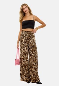 Zwarte cropped top, beige en donkerbruine wijde broek met luipaardprint, gladde textuur, hoog in de taille, accessoires met een roze handtas.