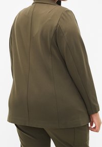 Blazer verde oliva, sartoriale, con maniche lunghe, taglio dritto e dettagli di cucitura minimal, realizzato in tessuto morbido. Adatto per diverse occasioni.