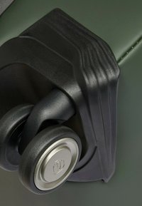 Zwart wielmechanisme bevestigd aan een groene harde koffer, met een strak ontwerp met ribbels en een metalen accent op het wiel.