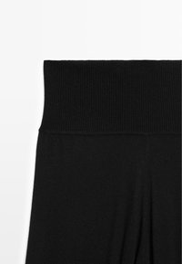 Schwarze Hose mit einem breiten, gerippten Bund und glatter Stoffstruktur. Das Material ist weich und dehnbar, was Komfort und Flexibilität ermöglicht.