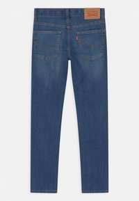 Mörkblå jeans i slim fit med två bakfickor och en brun läderlogotyp vid midjan. Slät textur.