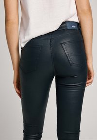 Pantalones ajustados azul oscuro con acabado brillante. Cuentan con dos bolsillos traseros y una cintura con una etiqueta de marca. Textura lisa en toda la prenda.