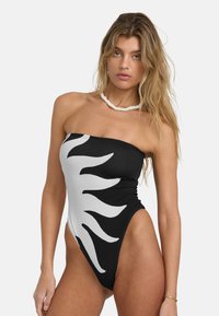 Svart-hvitt stripet stroppeløs badedrakt med solmotiv, høye benkutt og teksturert stoff. Pyntet med en perlekjede.