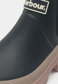 Καουτσούκ μπότες Barbour σε ναυτικό μπλε με λεία επιφάνεια. Διαθέτει ανοιχτό καφέ σόλα και εμφανές λογότυπο της μάρκας στο μπροστινό μέρος.