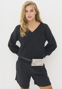 Black knitted pullover with a V-neck, textured shoulders, paired with black shorts and a silver, rhinestone-adorned belt pouch.
