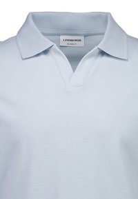 Polo bleu clair à coupe décontractée, doté d'un col classique et d'une fente à l'encolure ; texture douce en coton.