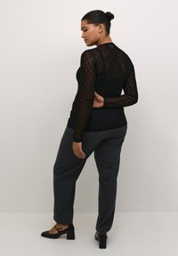 Top lung cu maneci lungi, transparent, de culoare neagră, cu buline texturate, asortat cu pantaloni tailoring de culoare gri închis și pantofi cu toc pătrat negri.