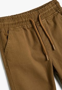 Brune elastisk pasform bukser med justerbar snor i livet, sidelommer og glat stoftekstur. Ingen mønstre eller yderligere hardware synlig.