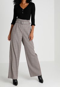 Czarny prążkowany top z długim rękawem i guzikami, zestawiony z szerokimi spodniami z wysokim stanem w brązowo-białą kratkę.