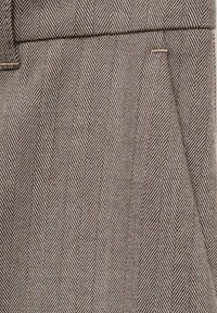 Stoff mit Fischgrätenmuster in Braun- und Beigetönen, der eine glatte Textur und einen subtilen Glanz aufweist, geeignet für Schneiderarbeiten oder formelle Kleidung.