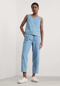 Light blue denim tank top worn with matching loose-fitting pants. Features a rounded neckline, front pockets, and cuffed ankles. White sneakers.