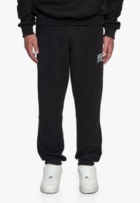 Sorte sweatpants lavet af blødt stof, udstyret med en elastisk talje og manchetter, med et hvidt logo-patch på venstre lår.