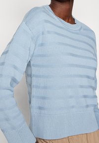 Maglione a righe blu chiaro, lavorato a maglia, con scollo rotondo, polsini e orlo a coste. Presenta bande testurizzate e una vita sagomata.