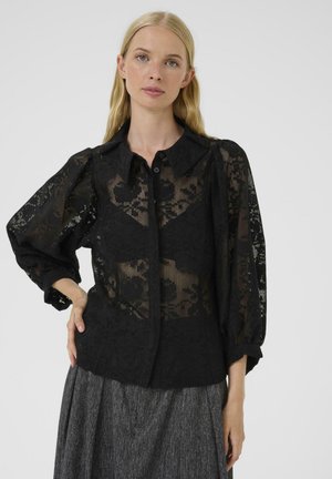Blusa nera in pizzo con collo a punta, chiusura a bottoni e maniche a palloncino, caratterizzata da motivi floreali e una texture trasparente.
