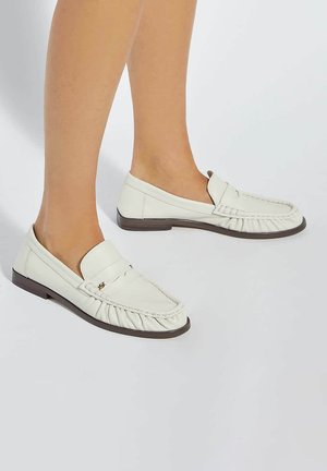 White leather loafers with a pleated design and rounded toe. Features a low, brown rubber sole and a decorative strap.