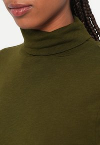 Olíva zöld garbó felső, puha, texturált anyagból készült, magas nyakkal és varrat nélküli vállkialakítással.