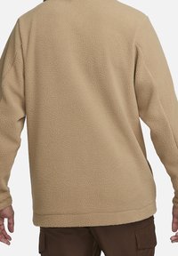 Beżowy polarowy pulower o teksturowanej powierzchni, z długimi rękawami i luźnym krojem. Posiada zaokrąglony kołnierz oraz dół sięgający nieco poniżej talii.