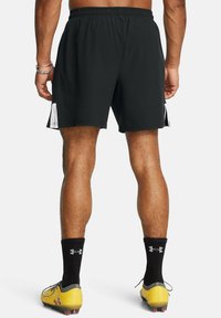 Pantalones cortos deportivos negros con un panel de malla, cinturilla elástica y dos bolsillos laterales. Llevados con zapatillas amarillas y calcetas negras.